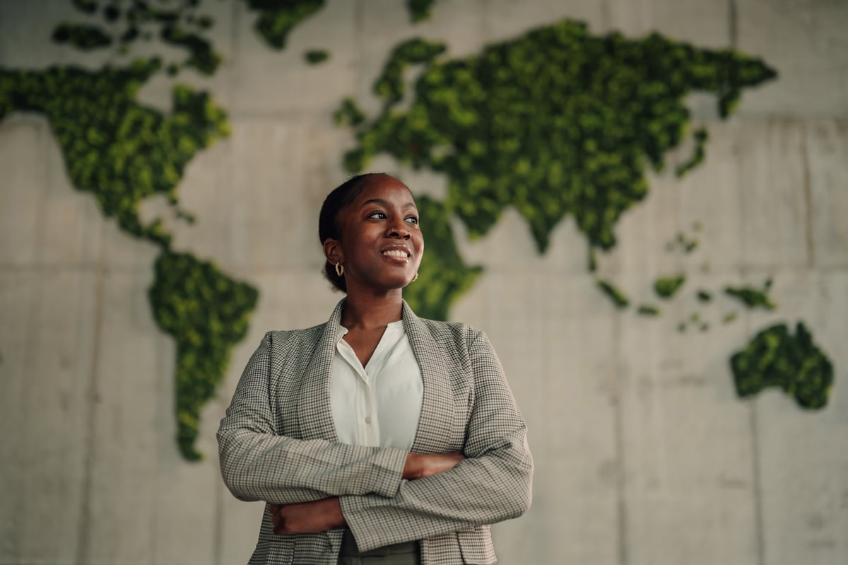 Confident businesswoman smiling, standing with arms crossed in front of a green moss world map, embracing global business leadership